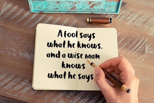 Retro effect and toned image of a woman hand writing on a notebook. Handwritten quote A fool says what he knows, and a wise man knows what he says as inspirational concept image