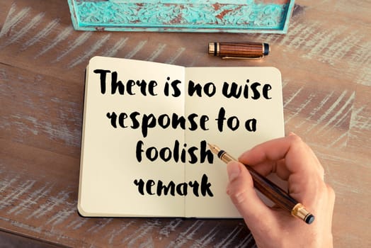 Retro effect and toned image of a woman hand writing on a notebook. Handwritten quote There is no wise response to a foolish remark as inspirational concept image