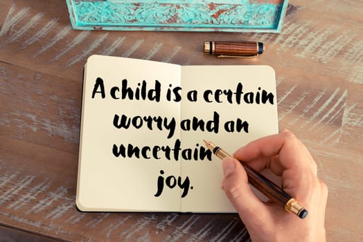 Retro effect and toned image of a woman hand writing on a notebook. Handwritten quote A child is a certain worry and an uncertain joy as inspirational concept image