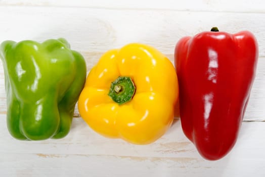 fresh yellow, red and green bell peppers on white wooden table