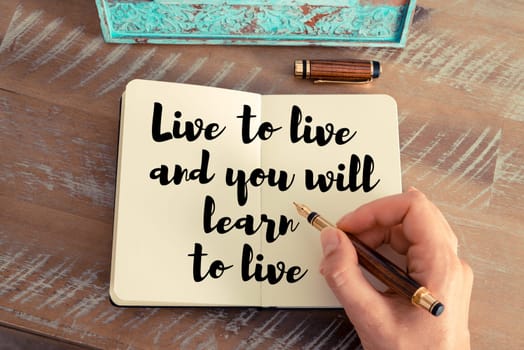 Retro effect and toned image of a woman hand writing on a notebook. Handwritten quote Live to live and you will learn to live as inspirational concept image