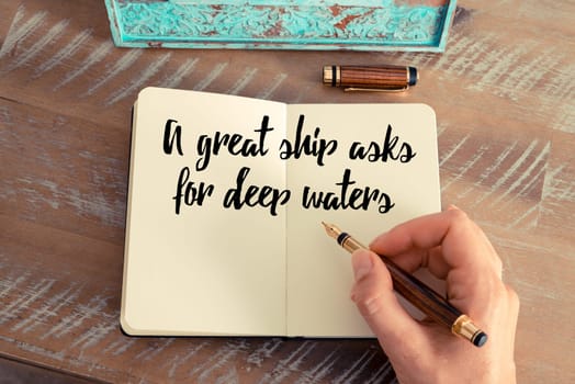 Retro effect and toned image of a woman hand writing on a notebook. Handwritten quote A great ship asks for deep waters as inspirational concept image
