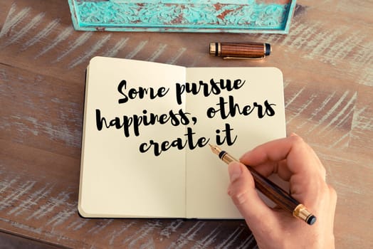 Retro effect and toned image of a woman hand writing on a notebook. Handwritten quote Some pursue happiness, others create it as inspirational concept image