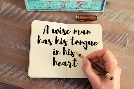 Retro effect and toned image of a woman hand writing on a notebook. Handwritten quote A wise man has his tongue in his heart as inspirational concept image