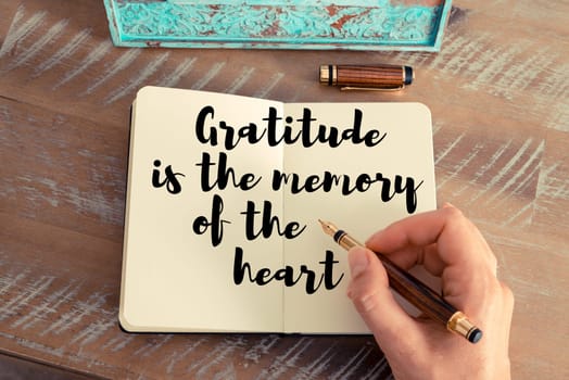 Retro effect and toned image of a woman hand writing on a notebook. Handwritten quote Gratitude is the memory of the heart as inspirational concept image