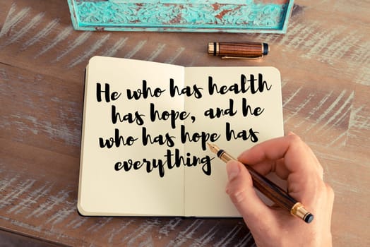 Retro effect and toned image of a woman hand writing on a notebook. Handwritten quote He who has health has hope, and he who has hope has everything as inspirational concept image