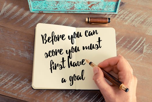 Retro effect and toned image of a woman hand writing on a notebook. Handwritten quote Before you can score you must first have a goal as inspirational concept image