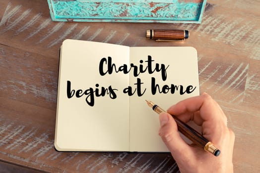 Retro effect and toned image of a woman hand writing on a notebook. Handwritten quote Charity begins at home as inspirational concept image