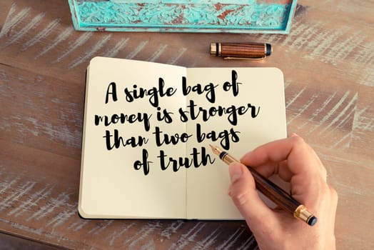 Retro effect and toned image of a woman hand writing on a notebook. Handwritten quote A single bag of money is stronger than two bags of truth as inspirational concept image