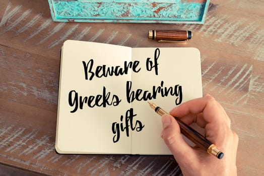 Retro effect and toned image of a woman hand writing on a notebook. Handwritten quote Beware of Greeks bearing gifts as inspirational concept image