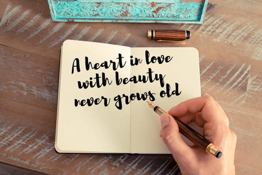 Retro effect and toned image of a woman hand writing on a notebook. Handwritten quote A heart in love with beauty never grows old as inspirational concept image