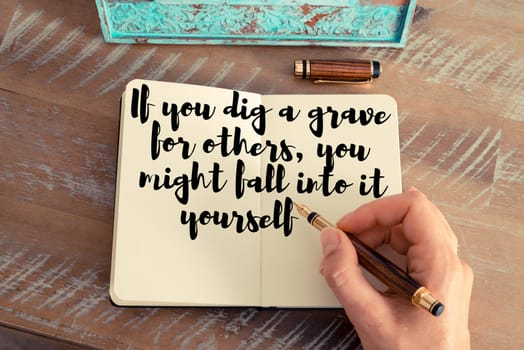 Retro effect and toned image of a woman hand writing on a notebook. Handwritten quote If you dig a grave for others, you might fall into it yourself as inspirational concept image