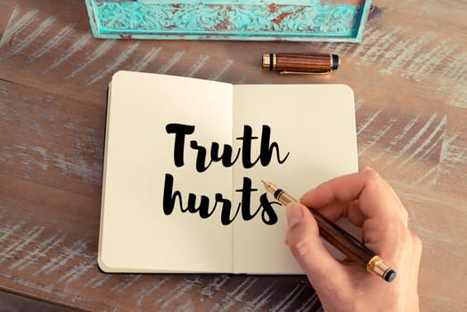 Retro effect and toned image of a woman hand writing on a notebook. Handwritten quote Truth hurts as inspirational concept image