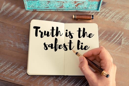 Retro effect and toned image of a woman hand writing on a notebook. Handwritten quote Truth is the safest lie as inspirational concept image