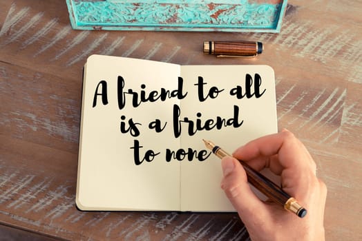 Retro effect and toned image of a woman hand writing on a notebook. Handwritten quote A friend to all is a friend to none as inspirational concept image