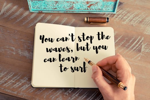 Retro effect and toned image of a woman hand writing on a notebook. Handwritten quote You can&#39 t stop the waves, but you can learn to surf as inspirational concept image