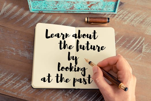 Retro effect and toned image of a woman hand writing on a notebook. Handwritten quote Learn about the future by looking at the past as inspirational concept image