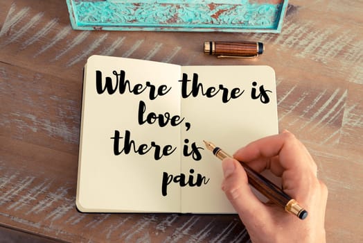 Retro effect and toned image of a woman hand writing on a notebook. Handwritten quote Where there is love, there is pain as inspirational concept image