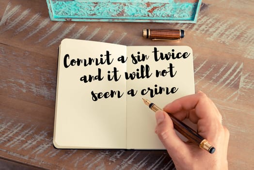 Retro effect and toned image of a woman hand writing on a notebook. Handwritten quote Commit a sin twice and it will not seem a crime as inspirational concept image