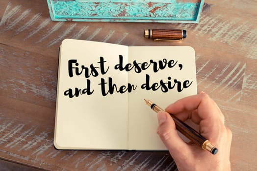 Retro effect and toned image of a woman hand writing on a notebook. Handwritten quote First deserve, and then desire as inspirational concept image