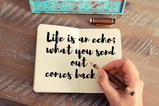 Retro effect and toned image of a woman hand writing on a notebook. Handwritten quote Life is an echo  what you send out comes back as inspirational concept image