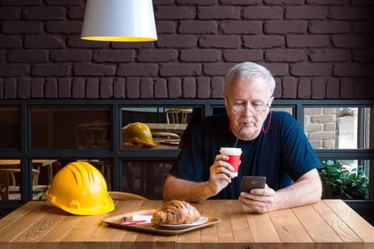 Senior construction foreman taking refreshment break, drinking coffee and checking his phone