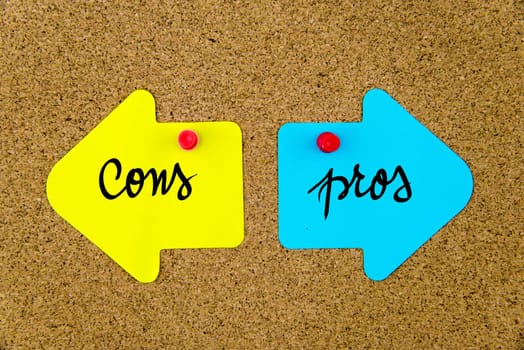 Blank yellow and blue paper notes in shape of opposite arrows pinned on cork board with thumbtacks, copy space available