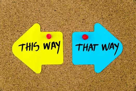 Blank yellow and blue paper notes in shape of opposite arrows pinned on cork board with thumbtacks, copy space available