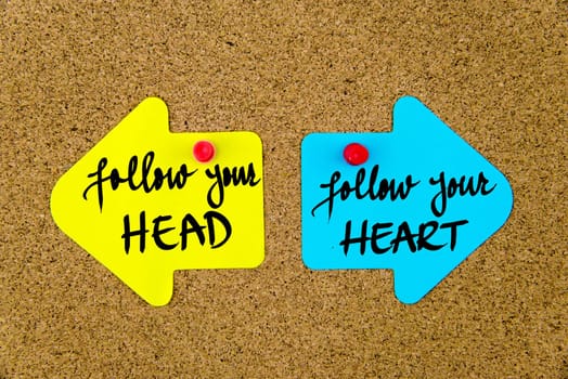 Blank yellow and blue paper notes in shape of opposite arrows pinned on cork board with thumbtacks, copy space available