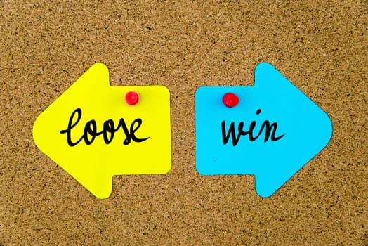 Blank yellow and blue paper notes in shape of opposite arrows pinned on cork board with thumbtacks, copy space available