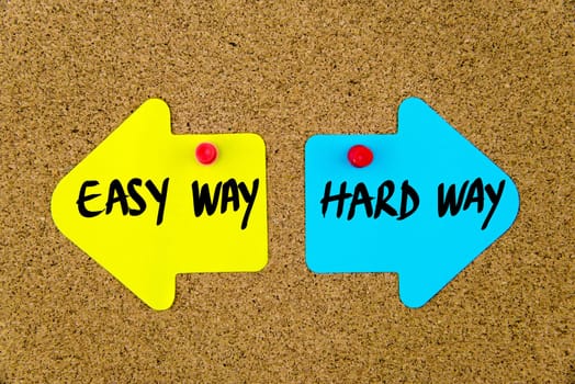 Blank yellow and blue paper notes in shape of opposite arrows pinned on cork board with thumbtacks, copy space available