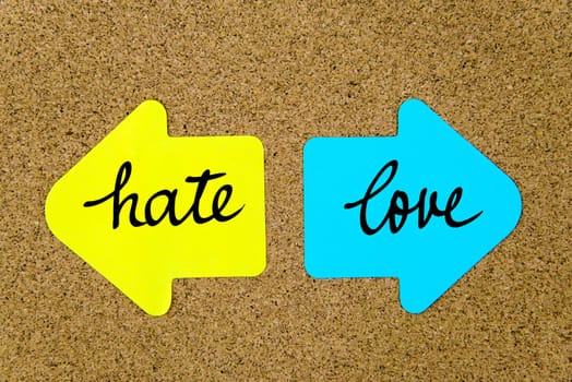 Message Hate versus Love on yellow and blue paper notes as opposite arrows pinned on cork board with thumbtacks. Choice conceptual image