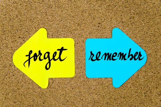 Message Forget versus Remember on yellow and blue paper notes as opposite arrows pinned on cork board with thumbtacks. Choice conceptual image