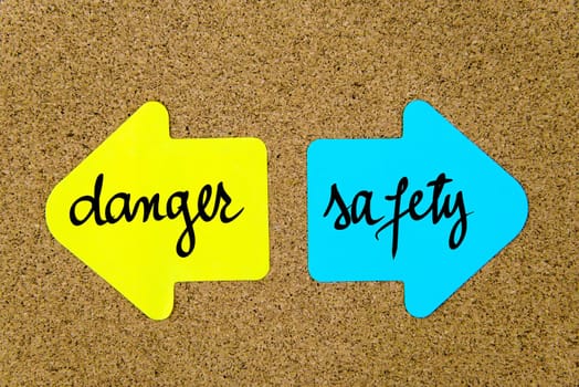 Message Danger versus Safety on yellow and blue paper notes as opposite arrows pinned on cork board with thumbtacks. Choice conceptual image