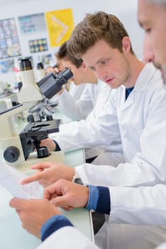 Students in lab using microscopes, reading paperwork