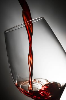 Close-up of filling a red wine glass in front of a lit studio background