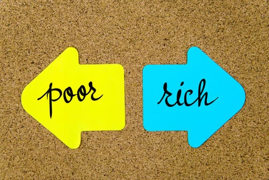 Message Poor versus Rich on yellow and blue paper notes as opposite arrows pinned on cork board with thumbtacks. Choice conceptual image