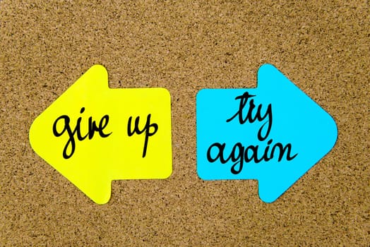Message Give Up versus Try Again on yellow and blue paper notes as opposite arrows pinned on cork board with thumbtacks. Choice conceptual image