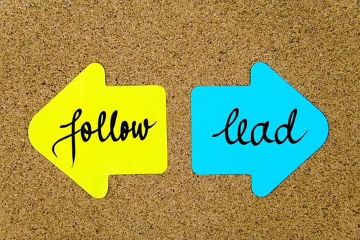 Message Follow versus Lead on yellow and blue paper notes as opposite arrows pinned on cork board with thumbtacks. Choice conceptual image