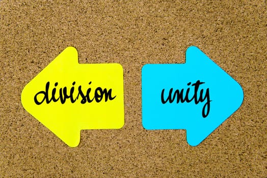 Message Division versus Unity on yellow and blue paper notes as opposite arrows pinned on cork board with thumbtacks. Choice conceptual image