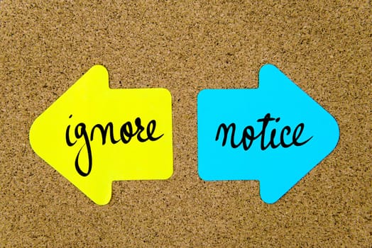 Message Ignore versus Notice on yellow and blue paper notes as opposite arrows pinned on cork board with thumbtacks. Choice conceptual image