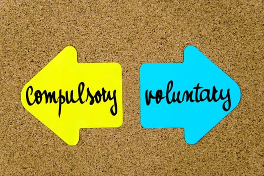 Message Compulsory versus Voluntary on yellow and blue paper notes as opposite arrows pinned on cork board with thumbtacks. Choice conceptual image