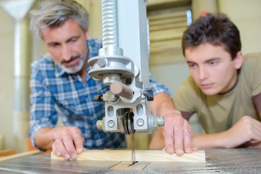 Carpenter teaching apprentice to use a bench saw