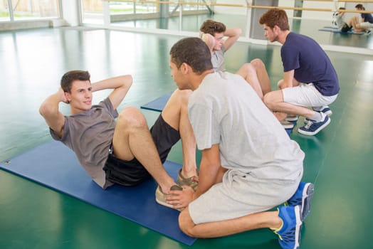 Two men holding feet of friends doing situps