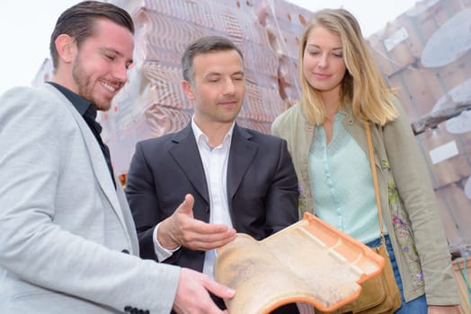 Salesman holding a modern rooftile for couple to see
