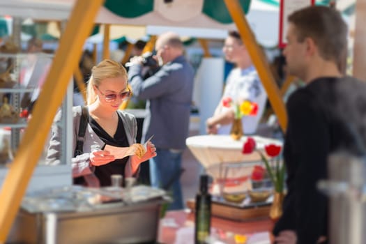 Beautiful blonde caucasian lady buying freshly prepared meal at a local street food festival. Urban international kitchen event in Ljubljana, Slovenia, in summertime.