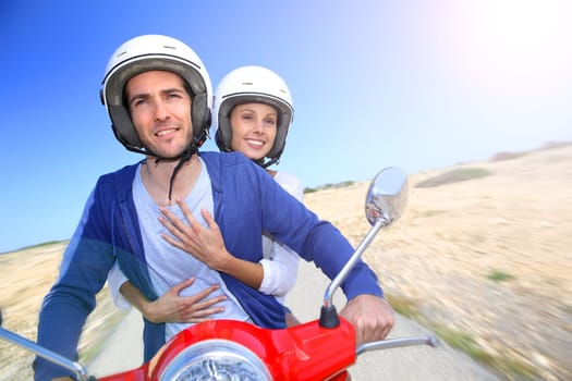Cheerful couple riding red moto on island