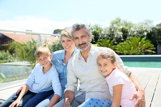 Happy family sitting by private swimming-pool