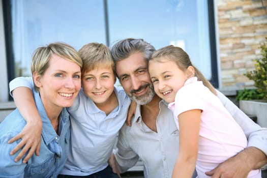 Happy family of four sitting in front of contemporary house