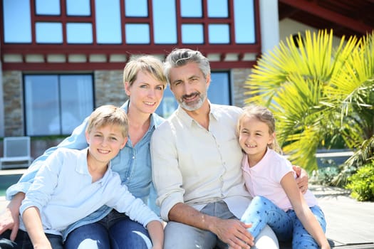 Happy family of four sitting in front of contemporary house